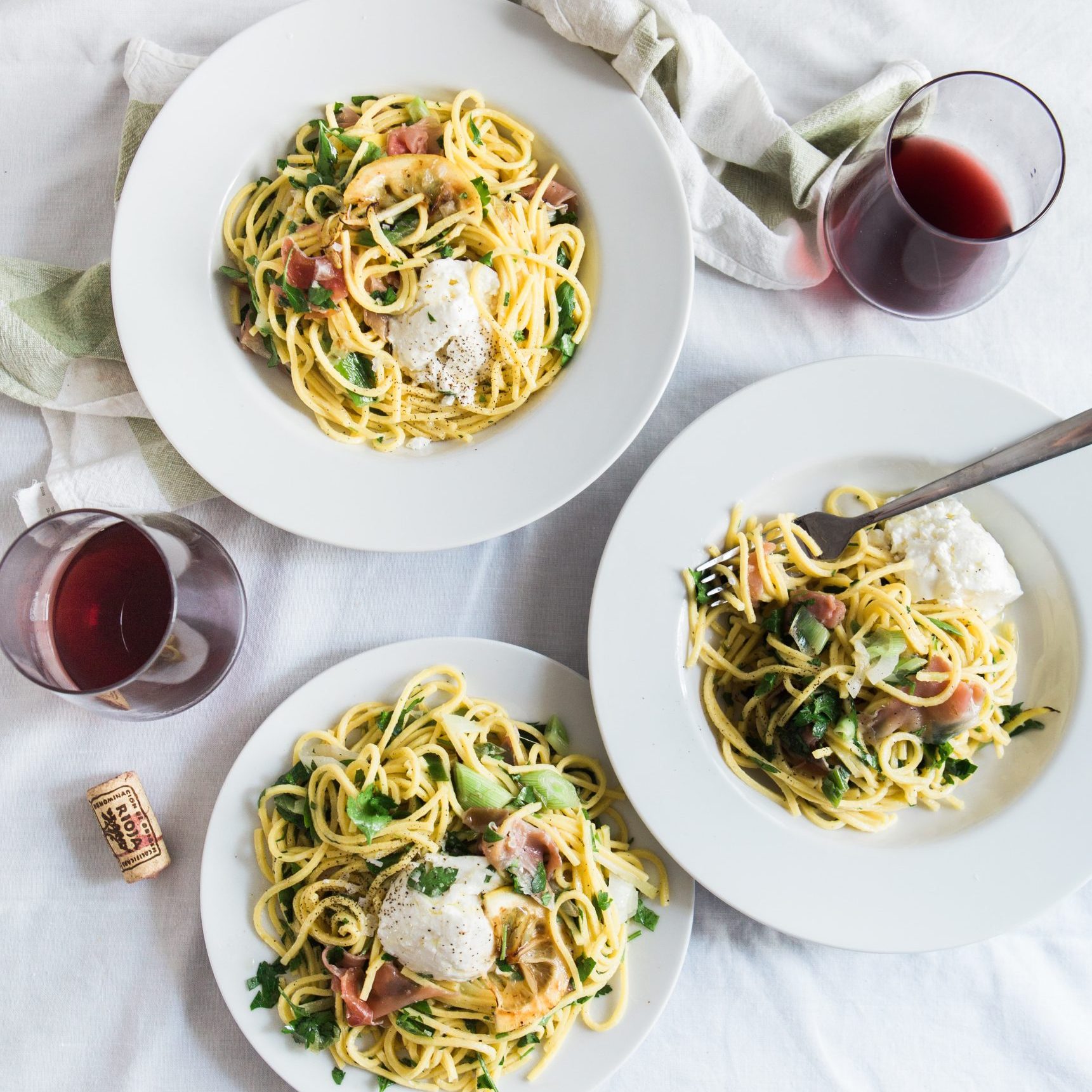 Three plates with pasta and wine on a bed.